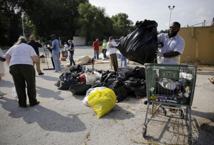 Volunteers help to cleanup trash behind a business Monday, July 27, 2015, in Ferguson, Mo. Hundreds of volunteers converged Monday morning on West Florissant Avenue for a litter-pickup and weeding effort spearheaded by a local radio station ahead of the Aug. 9 one-year anniversary of Michael Brown's death. It's one of the areas hardest hit by last year's unrest in Ferguson that followed the police shooting death of Brown. (AP Photo/Jeff Roberson)