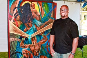 Artist, Kenneth L Carnes poses next to his painting, “Crack in the Foundation,” at the 49th annual Watts Summer Festival stage at Ted Watkins Park.