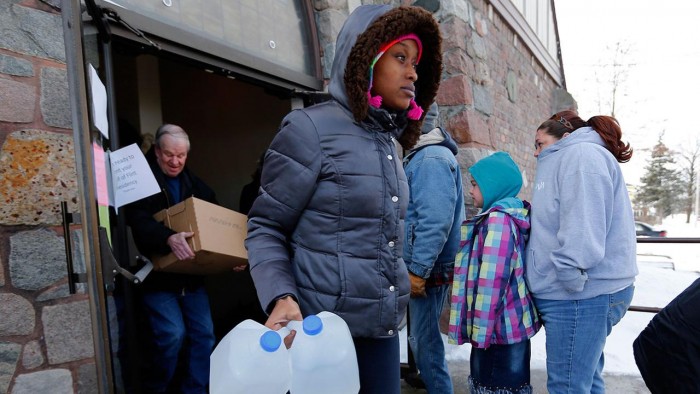 Genetha Campbell carries free water being distributed at the Lincoln Park United Methodist Church in Flint, Mich, (AP Photo/Paul Sancya)