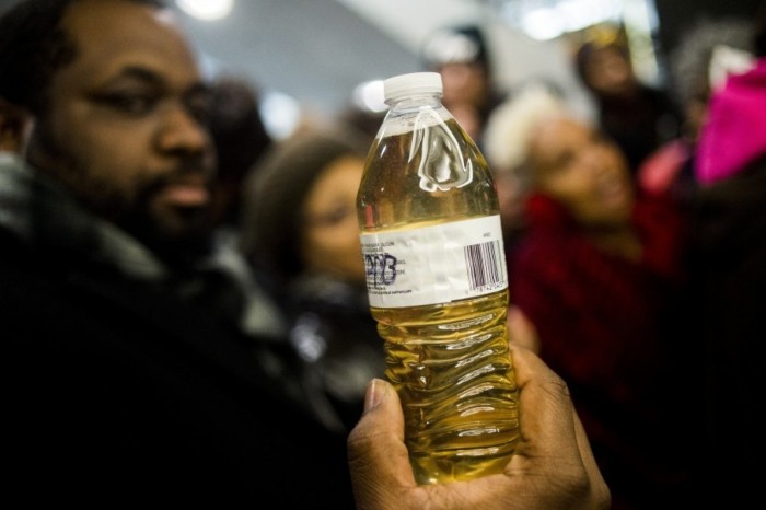 The Rev. David Bullock on Thursday holds a bottle of Flint water outside of the Romney Building, home to Gov. Rick Snyder’s office in Lansing. (Jake May/The Flint Journal-MLive.com/AP)