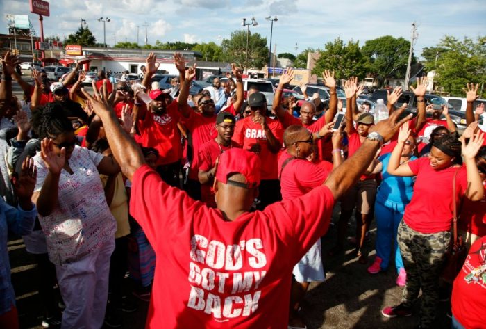 People pray for calm outside a business in Milwaukee, Sunday, Aug. 14, 2016. The business was burned during unrest after a police shooting. The black man whose killing by police on Saturday touched off rioting in Milwaukee was shot by a black officer after turning toward him with a gun in his hand, the police chief said Sunday, as Wisconsin's governor put the National Guard on standby against any further violence on the city's mostly black north side. (AP Photo/Jeffrey Phelps)