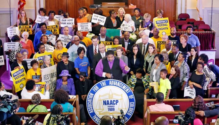 North Carolina NAACP president, Rev. William Barber, center at podium, gestures as he is surrounded by supporters during a news conference at the Third Street Bethel AME Church in Richmond, Va., Tuesday, June 21, 2016. The press conference was held to talk about the appeal before the 4th U.S. Circuit Court of Appeals on North Carolina's major rewrite of voting laws in 2013. (AP Photo/Steve Helber)