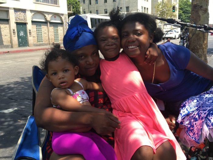 Andria Patterson and her children, 1-year-old Skylar, 6-year-old Nevaeh, and 15-year-old Sierra enjoy a moment of cool under a tree in front of Downtown L.A.'s Skid Row's Midnight Mission. (LAS photo/ Charlene Muhammad)