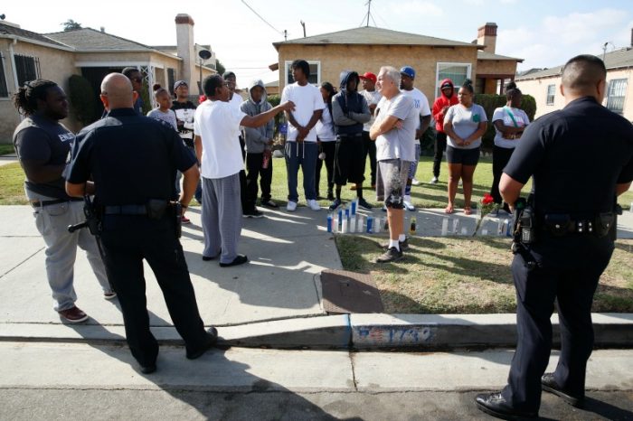 Los Angeles Police officers speak to neighbors and members of the community gathered around a makeshift memorial outside a residence on Sunday, Oct. 2, 2016. Officers shot and killed Carnell Snell Jr. in south Los Angeles on Saturday at the end of a car chase, sparking a protest by several dozen people angered by another fatal police shooting of a black man. (AP Photo/Damian Dovarganes)