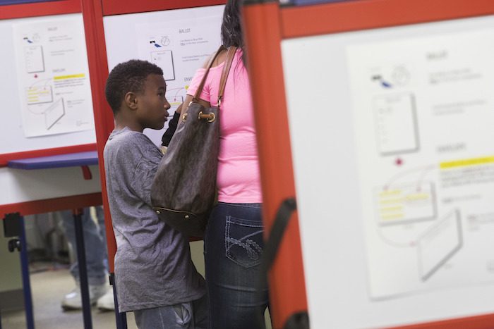 A young boy tags along at a voting booth as early voting beings at the Hamilton County Board of Elections, Wednesday, Oct. 12, 2016, in Cincinnati. (AP Photo/John Minchillo)